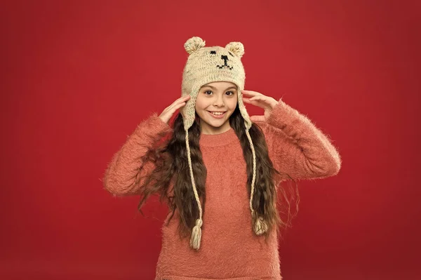 Μικρό κορίτσι αξεσουάρ χειμερινής μόδας. Μικρό παιδί μακριά μαλλιά φορούν καπέλο κόκκινο φόντο. Χαριτωμένο μοντέλο απολαμβάνουν το χειμώνα στυλ. Αξιολάτρευτο αρκουδάκι. Χειμερινή στολή. Το μικρό παιδί φοράει πλεκτό καπέλο. Μείνε ζεστή. — Φωτογραφία Αρχείου