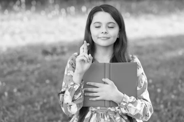 Ik doe een wens. Een klein kind kruist vingers voor geluk. Een klein meisje heeft een boek in het park. Volg je droom. Droom en fantasie. Zomervakantie. Droom een kleine droom — Stockfoto