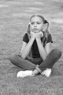 Küçük tatlı kız at kuyruğu saç stili yeşil çimlerde dinleniyor, hüzünlü gün konsepti.