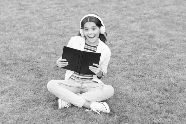 Jobba hårt. liten flicka läser bok. litteratur för barn. skriva barndomsminnen. Smart kille i headset. Tillbaka till skolan. Grabben studerar online i parken. lyssna musik på grönt gräs med bok — Stockfoto