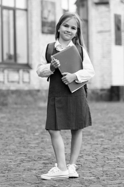 Щаслива маленька дитина в шкільній формі тримає бібліотечні книги на відкритому повітрі, день знань — стокове фото