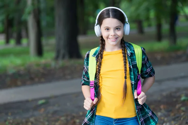 幸せな子供は、カジュアルファッションスタイルの自然な夏の風景で学校のバッグを運ぶ現代のヘッドフォンでオーディオコースに耳を傾け、聞いて — ストック写真