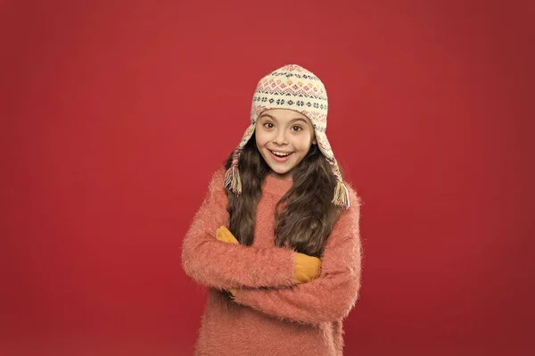 Clima helado. Traje de invierno. Lindo modelo disfrutar del estilo de invierno. Niño pequeño pelo largo usar sombrero fondo rojo. Concepto de invierno. Un niño pequeño usa un sombrero de punto. Niña accesorio de moda de invierno — Foto de Stock