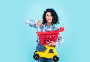 Kumral saçlı mutlu bir kadın günlük kıyafetler giyer alışveriş arabası taşır, satar.
