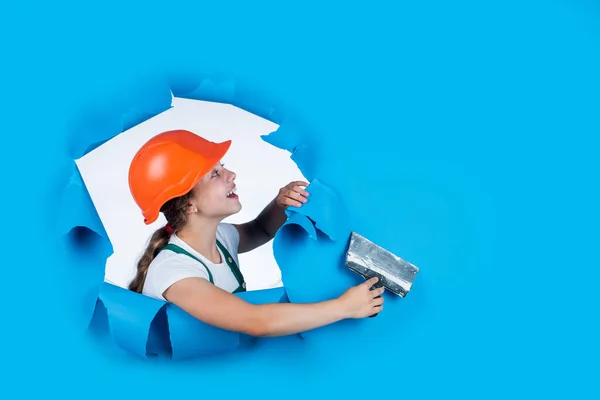 Ich brauche Hilfe. Kinder tragen auf der Baustelle Helm. Gipsermädchen mit Werkzeugspachtel. Kind bei Reparaturarbeiten. Konzept der Sanierung in der Werkstatt. Fleißiger Tischler mit Kelle — Stockfoto