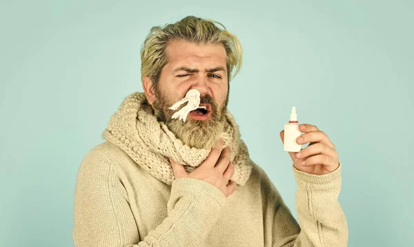 Man i halsduk hålla nässpray och näsduk. Kalla influensabehandlingar. rinnande näsa och andra förkylningssymtom. injicera droppar i näsan. Coronavirus från Kina. Försöker att inte nysa. ammar förkylning eller allergi i näsan — Stockfoto