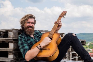 Uzun saçlı hippi ve bıyıklı gitarist. Müzik aleti olan erkek gitarist. Country müzik konsepti. Sakallı adam akustik gitar çalar. Adam insani duygularını ifade ediyor. # Kendini bırak havaya #