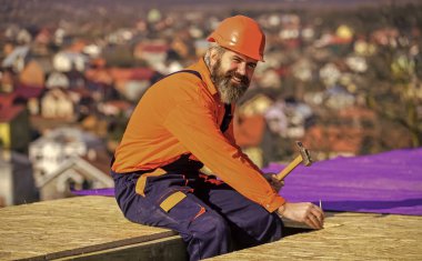 Yakışıklı inşaatçı çekiç kullanır. Profesyonel tamir çatısı. Düz çatı kurulumu. Çatı keçesi. Özel koruma giysisi içinde çatı tamircisi. İnşaat binasının altındaki yeni çatı