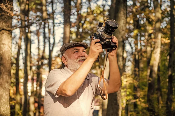 La mejor cámara para profesionales. Antiguo fotógrafo en el día de otoño. Pensionista mantenga la cámara vintage en el bosque. Un anciano con cámara fotográfica. Usando cámara analógica para disparar. Sesión de sesión de fotos naturaleza — Foto de Stock