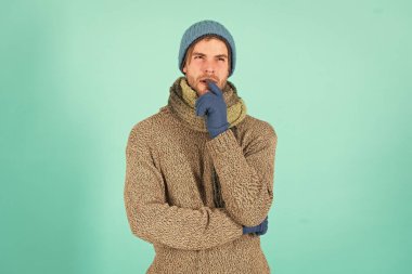 Peki ya... Tıraşsız yakışıklı adam mavi arka planda kış aksesuarları takıyor. Kış sezonu indirimi. Hippi, kış şapkası eşarbı ve eldiven ördü. Duygusal bir ifade. Düşün ve karar ver. Zor karar.