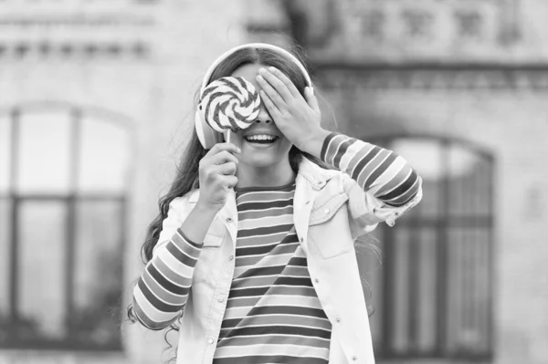 女の子のワイヤレスヘッドフォンは、ロリポップキャンディー、ブラインド選択の概念を食べる — ストック写真