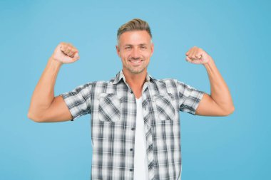 Yapabilirim. Güçlü adam mavi arka planı. Kaslı adam kollarını esnetir. Sıradan tarzda yakışıklı bir adam. Beyaz adam güç gösterisi yapıyor. Moda ve tarz. Spor ve spor salonu. Antrenman ve antrenman