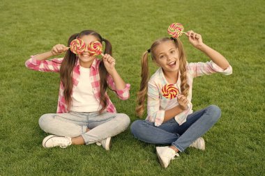 Tatlı çocukluk. Mutlu çocuklar şeker tutarken yeşil çimlerde otururlar. Şekerci. Lolipop ikramları. Şeker mutluluğun eşanlamlısıdır. Şeker ve kalori. Neşeli neşeli arkadaşlar dışarıda tatlı yiyorlar. Tatil yemeği.