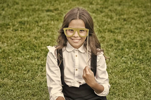 Τελευταία μέρα στο σχολείο. Ευτυχισμένο κορίτσι κρατήσει στηρίγματα γυαλιά πράσινο γρασίδι. Μικρό παιδί με σχολική εμφάνιση. Σχολική μόδα και αξεσουάρ. Αποχαιρετιστήριο πάρτι σχολείου. Τελευταίο χτύπημα καμπάνας, φίλτρο εποχής — Φωτογραφία Αρχείου