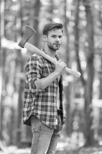 Hombre barbudo en camisa a cuadros con pantalones vaqueros llevan hacha de división grande en el ambiente natural de madera de verano, leñador —  Fotos de Stock