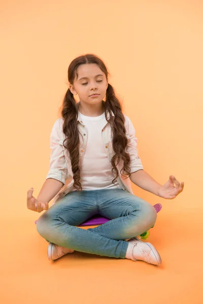 Dziewczyna medytuje siedząc na tablicy na żółtym tle. Małe dziecko zrelaksować się na deskorolce. Czas na jogę. Koncentracja i medytacja. Żyć w spokoju i deskorolce — Zdjęcie stockowe