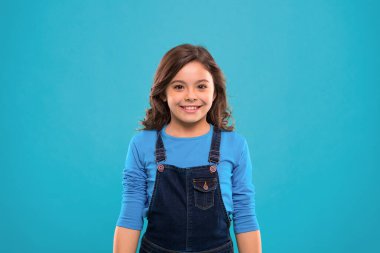 Saf güzellik. Uzun, sağlıklı, parlak saçlı kız günlük kıyafetler giyiyor. Uzun saçlı küçük kız. Mavi arka planda sevimli kıvırcık saçlı çocuk. Düzenli saçlar için güzel ipuçları