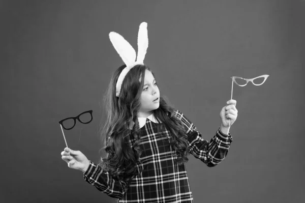Это трудный выбор. Счастливой Пасхи. Маленькая девочка носит кроличьи уши на Пасху. серьезный ребенок выбирает очки для вечеринок. Пасхальный кролик с ушами. подросток в кроличьем костюме веселится — стоковое фото