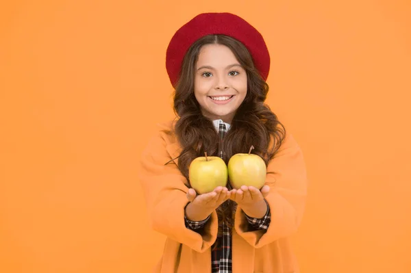 Вітамін починається зі шкільного року. Щаслива дівчина тримає вітамінні фрукти жовтого фону. Маленька дитина посміхається зеленими яблуками. Здоровий вітамінний перекус. Шкільне здоров'я. Найкращі джерела вітаміну — стокове фото