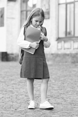 Resmi üniformalı küçük bir çocuk okul kitaplarını açık havada, kütüphanede tutuyor.