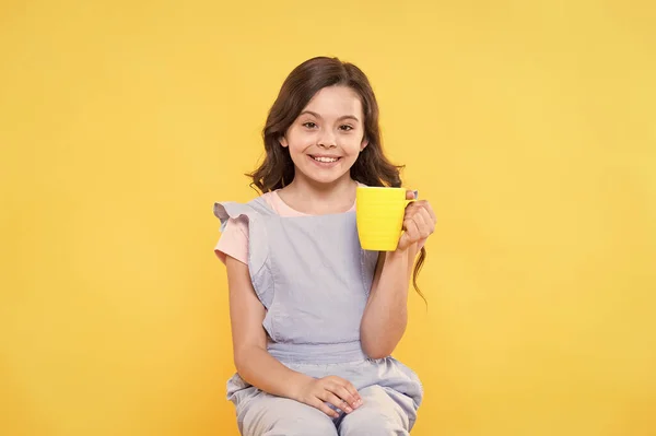 Νόστιμο τσάι με γάλα. Ευτυχισμένο παιδί κρατήσει φλιτζάνι τσάι κίτρινο φόντο. Το κοριτσάκι απολαμβάνει να πίνει τσάι. Ζεστό ποτό. Πρωινό ποτό. Ώρα για πρωινό. Καλή συνήθεια. Η ευτυχία είναι ένα φλιτζάνι τσάι — Φωτογραφία Αρχείου
