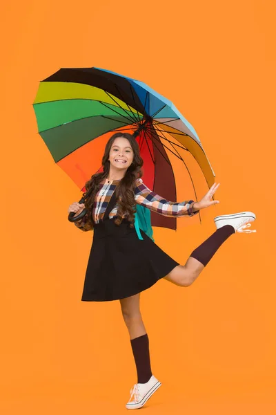 По дорозі до школи. Весела усміхнена школярка. Дощовий день весело. Щаслива прогулянка під парасолькою. Насолоджуйтесь концепцією дощу. Дівчинка щаслива тримає барвисту парасольку веселки. Дощова погода з правильним одягом — стокове фото