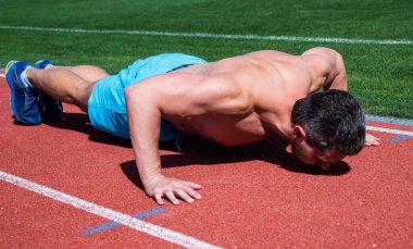 Atletik kaslı adam stadyumda şınav çekiyor.