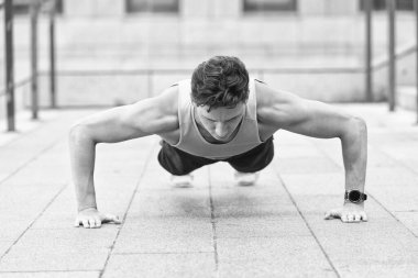 Beyaz tenli sporcu şınav çekiyor. Fitness antrenmanı. Açık havada şınav çek. Spor kıyafetli genç yakışıklı şınav çekiyor. Baldır ve kalça kasları için egzersiz yapıyor. mekik çeken yakışıklı adam.