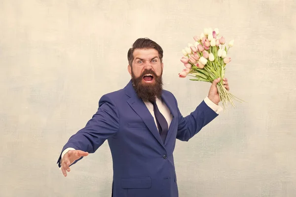 Hate holidays. Womens day. March 8. Angry bearded man with flowers. Celebrate spring. Date failure. Irritated annoyed aggressive bearded man with tulip bouquet. Disappointed concept. Failed date
