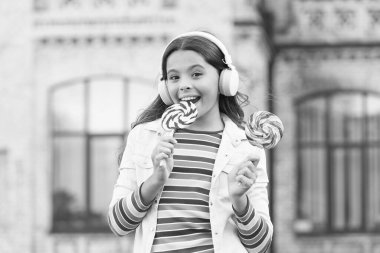 Neşeli kız modern kablosuz kulaklıklar şeker yer, lezzetli lolipop konsepti