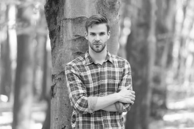 Ağacın yanındaki genç adam kareli gömlek giyiyor, gündelik moda.