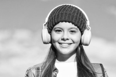 Çocuklarını kulaklarından koru. Mutlu kız güneşli mavi gökyüzünde kulaklık takıyor. Küçük çocuk kulaklıkla müzik dinler. Kulak ve işitme bakımı. Modern hayat. Yeni teknoloji. Seni eğlendirir ve güvende tutar.