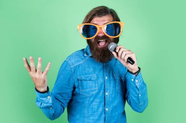 Yüksek sesle konuş. Mikrofonlu erkek hoparlör. Sesli. Mutlu gülümseyen olgun adam. Sakallı adam mikrofonda şarkı söylüyor. Vahşi Kafkas hipster etkinlik yöneticisi. Komik parti gözlükleri. karaoke ve müzik