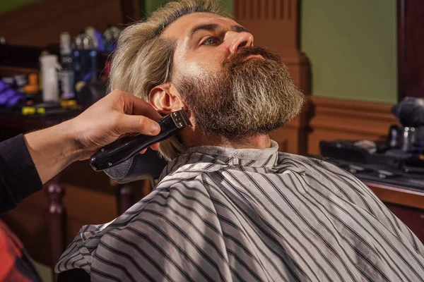 Shaving with electric razor. mature man at barbershop. brutal bearded man at hairdresser. professional barber with male client. hipster with dyed beard and moustache. man want new hairstyle