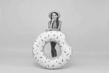 Yaz plajı aktivitesi. Mutlu çocukluk. Küçük kız hasır şapka ve mayo giyiyor. Sarı arka planda gülümseyen bir çocuk. Tatil ve tatil. Havuz partisi. Lastik halkalı kaygısız çocuk.