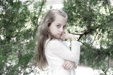 Yaz mevsiminde yeni bir cilde sahip çocuk manken. Moda elbiseli kız yeşil ağaçta poz veriyor. Açık havada uzun sarı saçlı küçük bir çocuk. Moda güzelliği ve saç stili. Cilt bakımı ve tazeliği