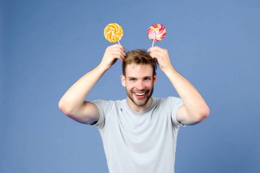Kafasında mor arka planda lolipoplar olan komik bir adam. Mor arka planda çubuklardaki şekerlemelerle maço bir gülümseme. Mavi tişörtlü, kıvrımlı karamelli manken. Yemek, atıştırmalık ve tatlı yemek.