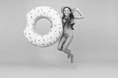 seyahat konsepti. Sarı arka planda zıplayan çocuk. Tatil ve tatil. Havuz partisi. Lastik halkalı kaygısız çocuk. Yaz plajı aktivitesi. Mutlu çocukluk. Küçük kız hasır şapka ve mayo giyiyor.