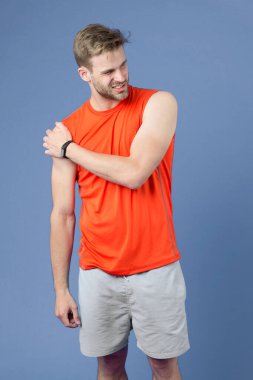 Sporcu menekşe arka planda omuza dokunuyor. Kaslı adam antrenmandan sonra ya da antrenmandan sonra acı hisseder. Omzum ağrıyor. Spor sakatlığı. Masaja ihtiyacım var. Sağlık ve tedavi. Vücut bakımı ve sağlık