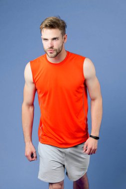 Seksi kaslı vücutlu bir sporcu. Maraton, spor ve spor konseptinden önce koşuculuk eğitimi. Süslü sakallı, turuncu yelek ve mavi şort giyen bir adam. Sporcu mor arkaplanda izole edildi