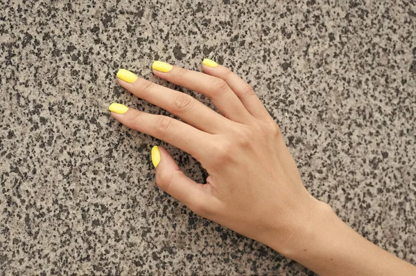 Professional nail care. Female hand with yellow nail color. Applying nail lacquer. Nail salon manicure. Acrylic overlays and extensions. Cosmetic beauty treatment for fingernails