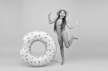 Eğlenceli bir aksesuar. Mutlu çocukluk. Küçük kız hasır şapka ve mayo giyiyor. Sarı arka planda gülümseyen bir çocuk. Tatil ve tatil. Havuz partisi. Lastik halkalı kaygısız çocuk. Yaz plajı aktivitesi