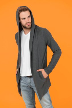 Sportif tarzda. Günlük yaşam için rahat kıyafetler. Moda adamı sarı arka plan. Moda bakışı. Yakışıklı adam kapüşonlu şık bir manto giyiyor. Erkekler için günlük kıyafet. Moda trendleri. Gençler için modern kıyafetler
