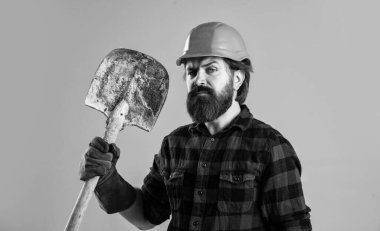 Kasklı inşaat işçisi. Güvenlik miğferi takmış mühendis. Acımasız teknisyen. Fabrika işçisi tamircisi. Kasklı endüstriyel işçi. Adam eldiven içinde kürek tutuyor.