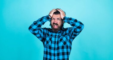 Başım ağrıyor. Modern görünümlü sakallı hippinin başı ağrıyor. Sağlık hizmeti konsepti. Bıyıklı vahşi yakışıklı adam. Mavi arka planda olgun bir berber. Erkeklik ve karizma. Hayır.