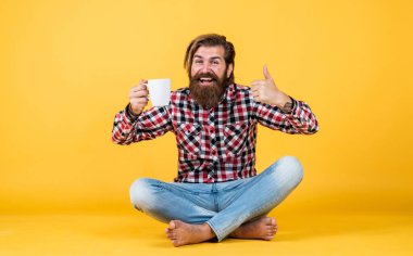 Bunu dene. Adam fincandan sıcak çay içiyor. Günaydın. Enerjik, sıcak bir içecek. İlham için kahve. Güne mükemmel bir başlangıç. Mutlu sakallı adam sabah kahvesini içiyor. En iyi tat için başparmağınızı kaldırın
