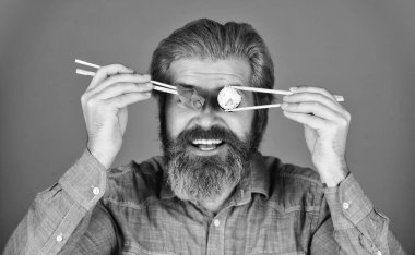 Adam suşi çubuğu yiyor. Japon mutfağı. Asya yemeği. Suşi rulosu. Suşi ruloları. Doğu kültürü. Sakallı hippi rulo yiyor. Japon yemek teslimatı. Suşi ya da sashimi ile servis edilen zencefil turşusu.