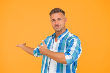 Yaz satışları burada. Seksi adam sarı arka plan. Olgun, tıraşsız bir adam. Gülümseyen adam parmakla işaret ediyor, kopyalama alanı. Erkek model bahar tişörtü. Ürün sunumu. Erkekler için eşyalar. mevsimlik indirimler