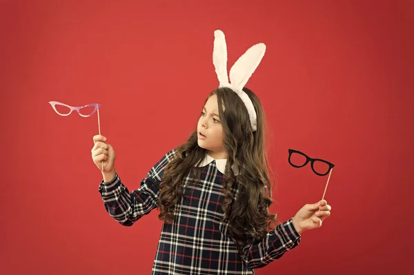 this is hard choice. happy easter. small girl wear bunny ears on Easter day. serious child choose party glasses. Easter bunny rabbit with ears. teen kid in rabbit costume having fun