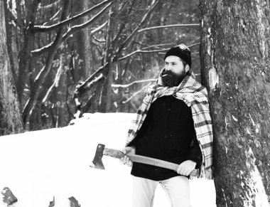 Yakışıklı bir adam ya da oduncu, sakallı hippi, sakallı ve bıyıklı, ekose battaniyeye sarılı, karlı ormanda ağaçların altında baltayla duruyor.